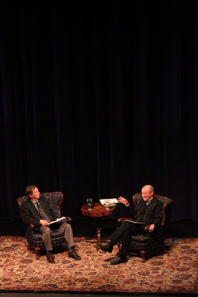 Dean Nelson talks with a writer while they each sit in comfy arm chairs.