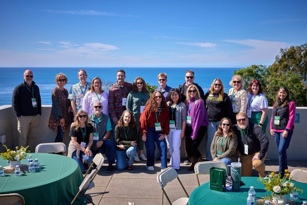 A PLNU Homecoming reunion group gathers for a group photo with the bright blue ocean behind them