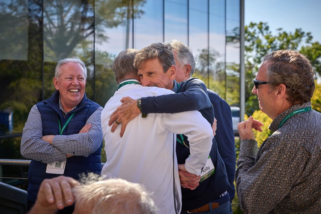 Two male PLNU alums greet each other at Homecoming with a big hug.