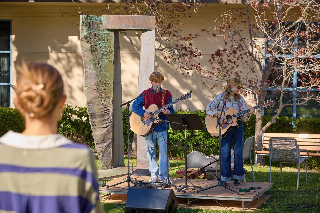 Two students play acoustic guitar outside at Homecoming