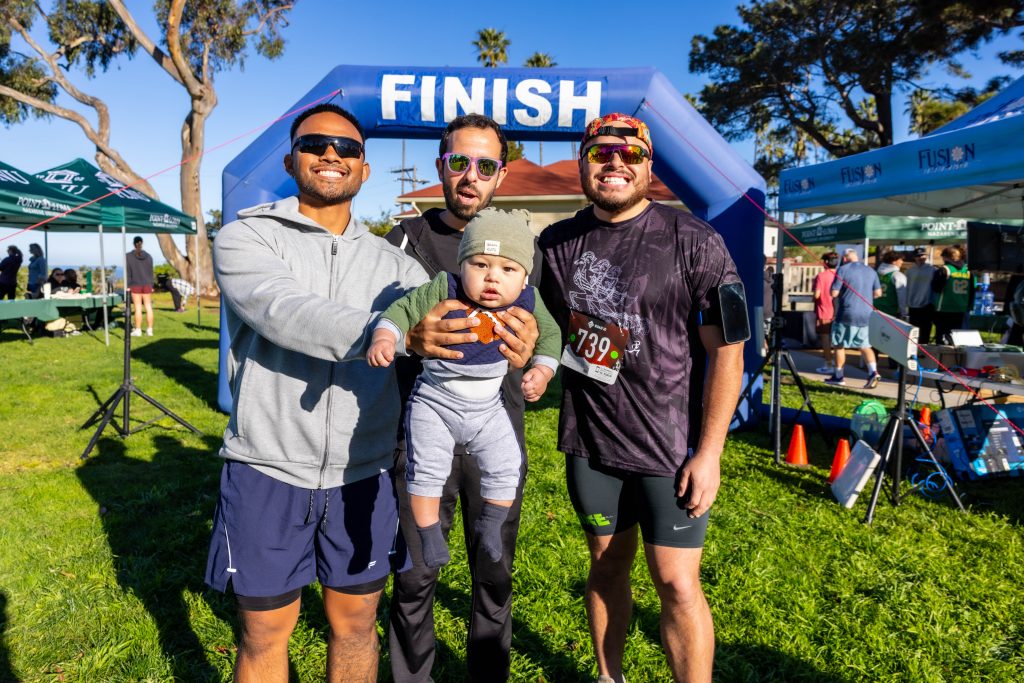 Three PLNU friends and a baby gear pose at the finish line of the Homecoming 5K.