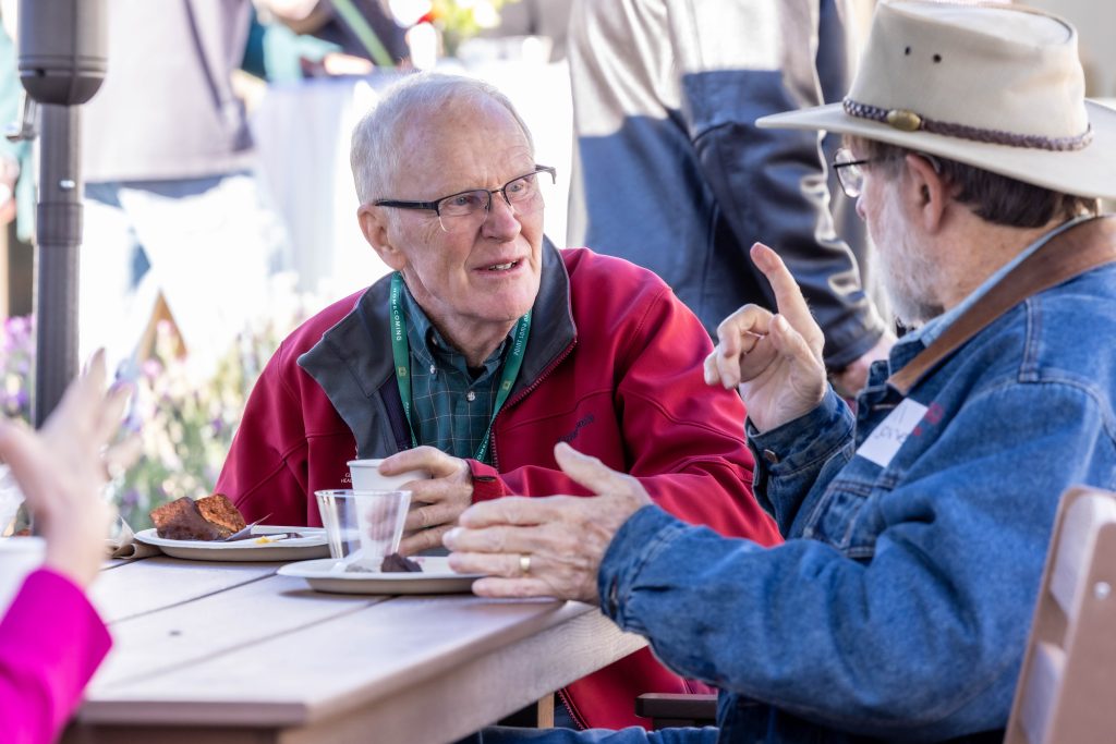 Two older PLNU alums reconnect at a table during Homecoming.