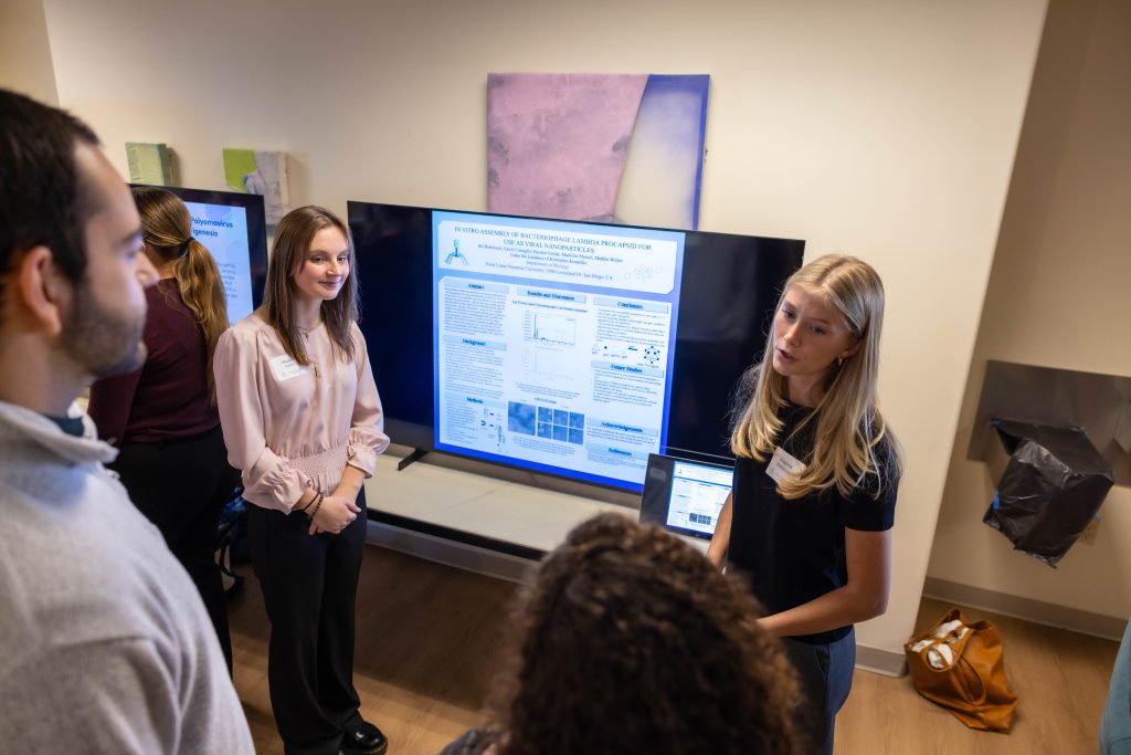 PLNU science students present their research on a tv screen to alums.