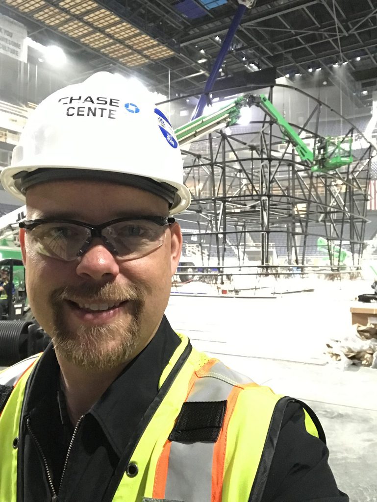 Heitman stands with an engineered structure behind him wearing a construction uniform. 